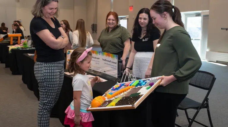 A group of students share a sensory texture board with a young girl at an Autism Expo