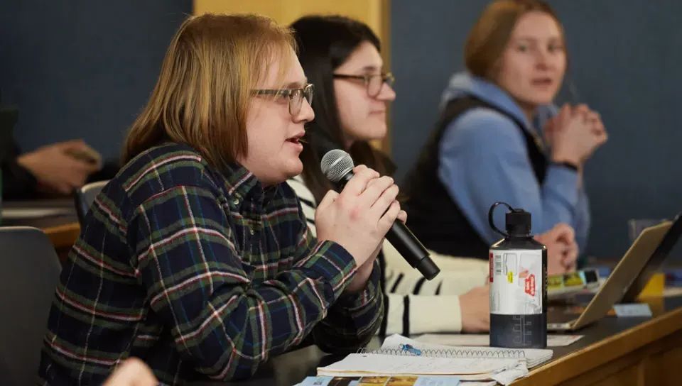 A U N E student holds a microphone as they ask a question from the audience of a C G H lecture